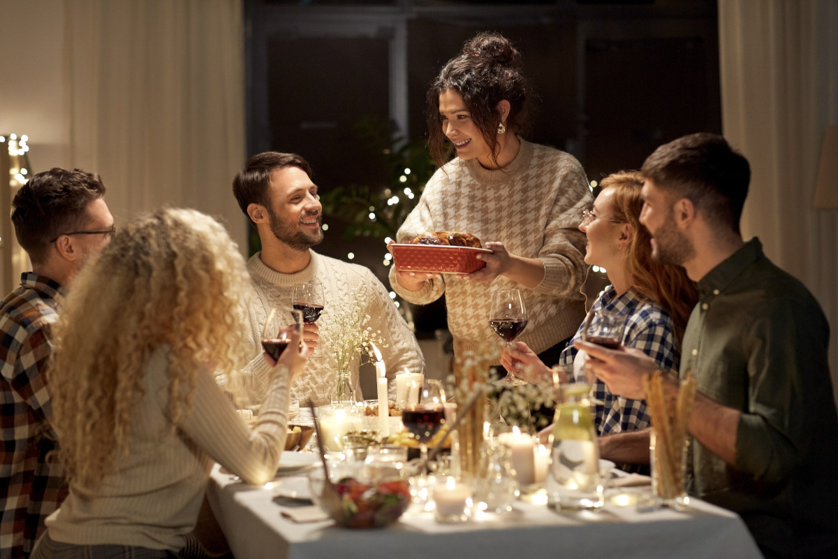Friends laugh around a dining table decorated for Christmas.