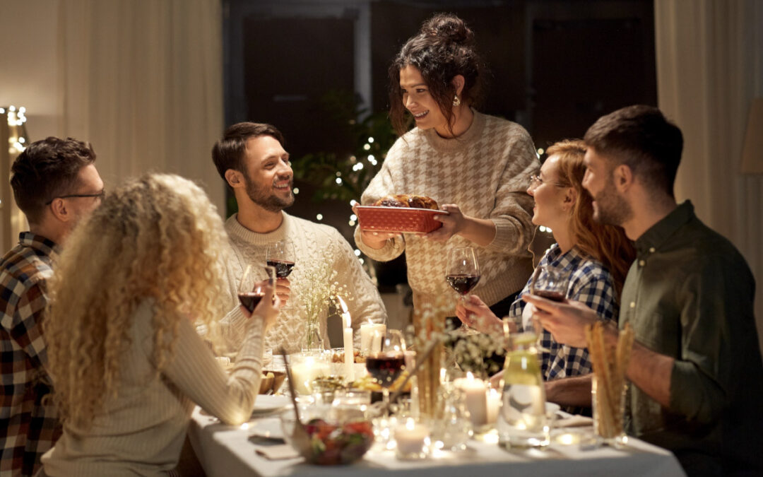 A host places food on a dining table with her friends.