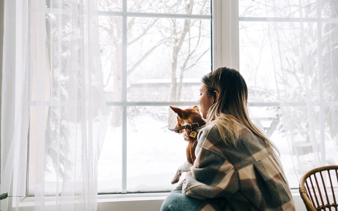 Woman and her dog gazing out of rental window at the snow.
