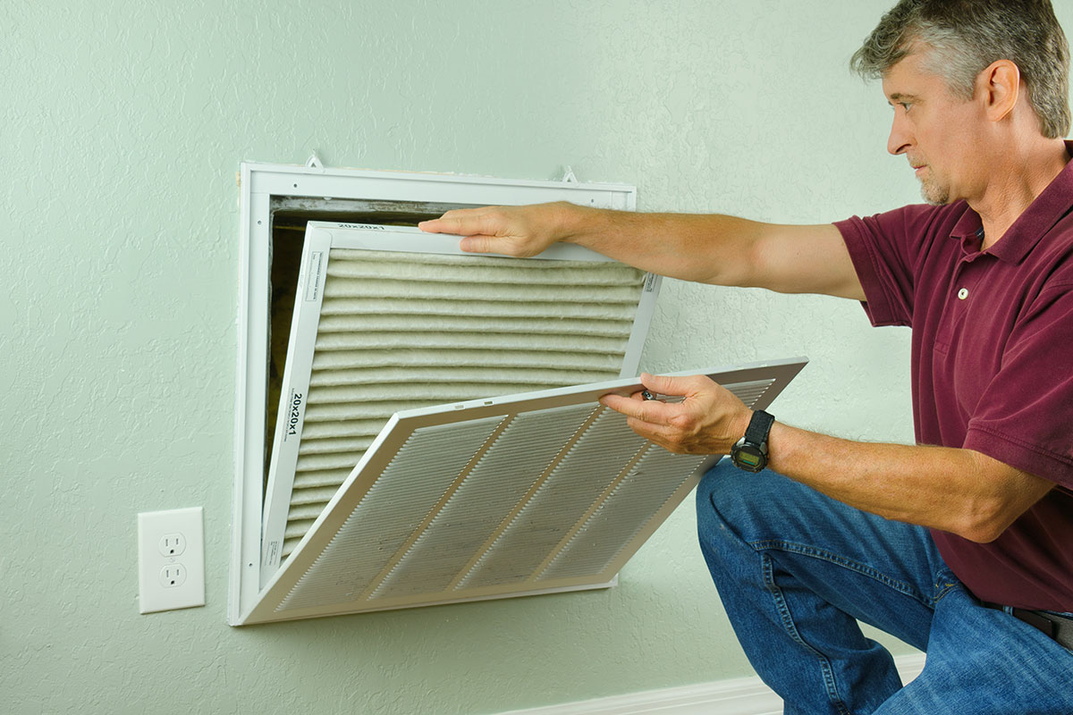 Maintenance man changing HVAC filter in apartment.