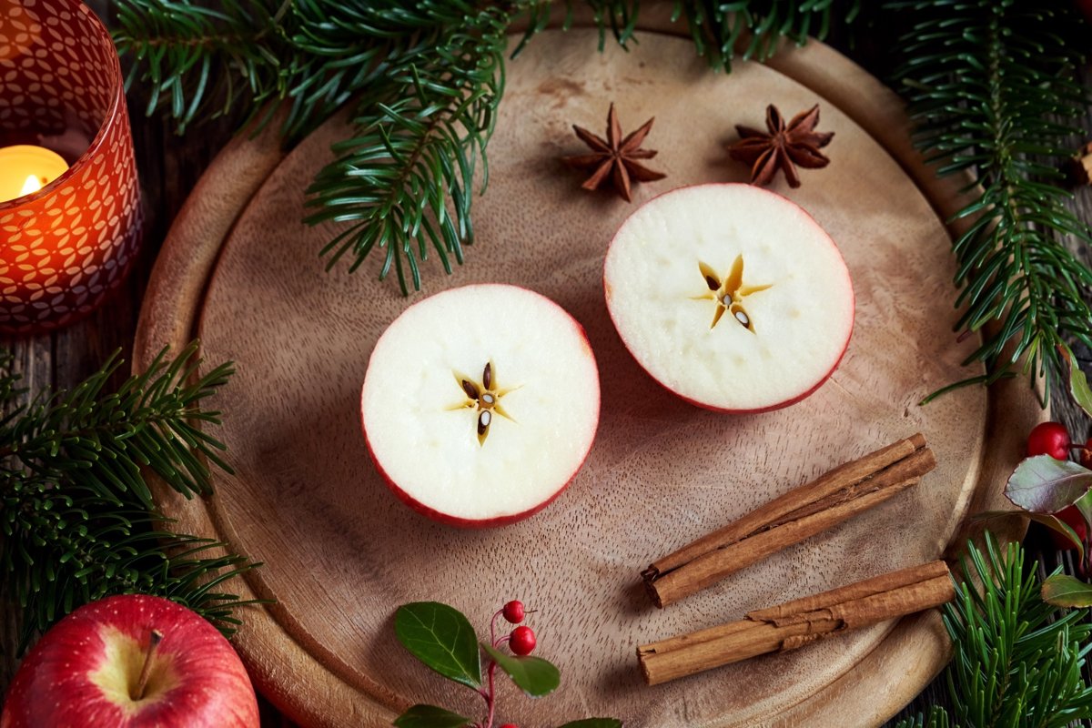 A table featuring a cut apple, cinnamon sticks and green sprigs surrounded by a lit candle.