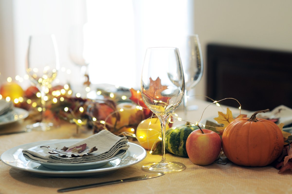 A long line of pumpkins and leaves placed in the center of a dining room table accented with fairy lights for a warm glow.