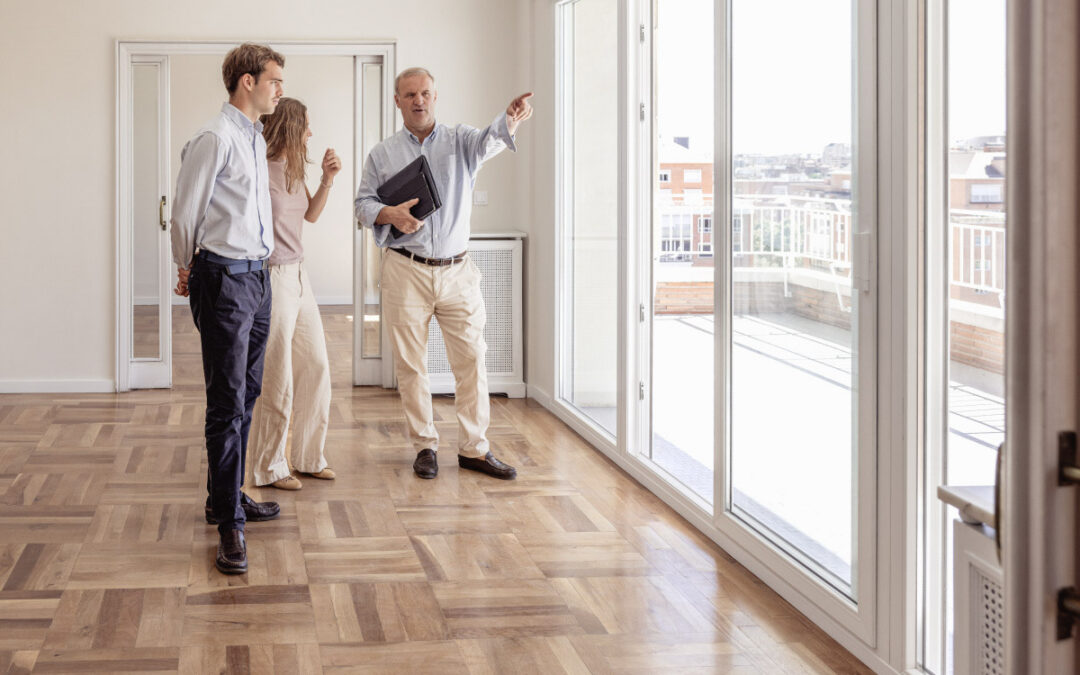 A leasing agent showing a spacious apartment with a large balcony to a young couple.
