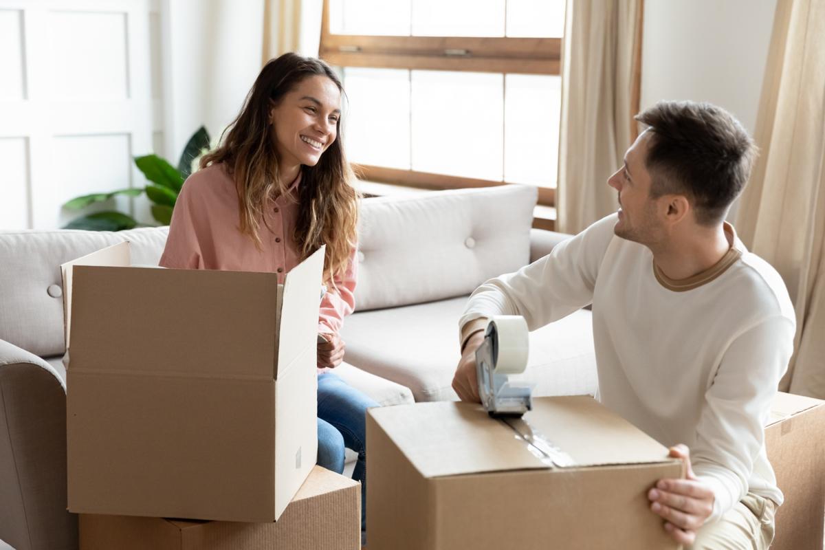 Young couple taping and packing moving boxes together in a cozy living room — moving into a new apartment.
