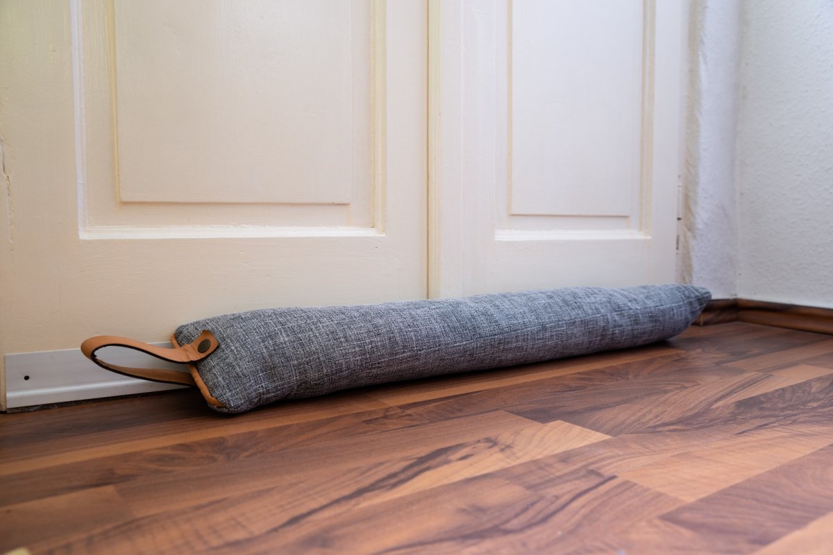 A long filled tube of fabric on the floor set in front of a door to keep the cold air from seeping in.