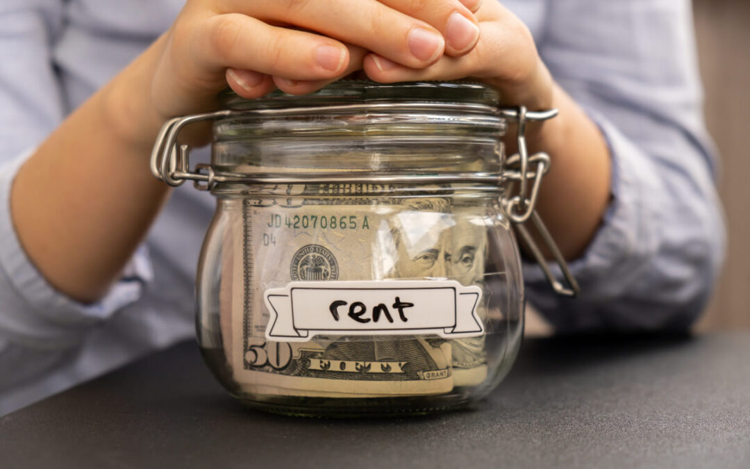 Pair of hands on top of jar that has money in it and is labeled "rent."