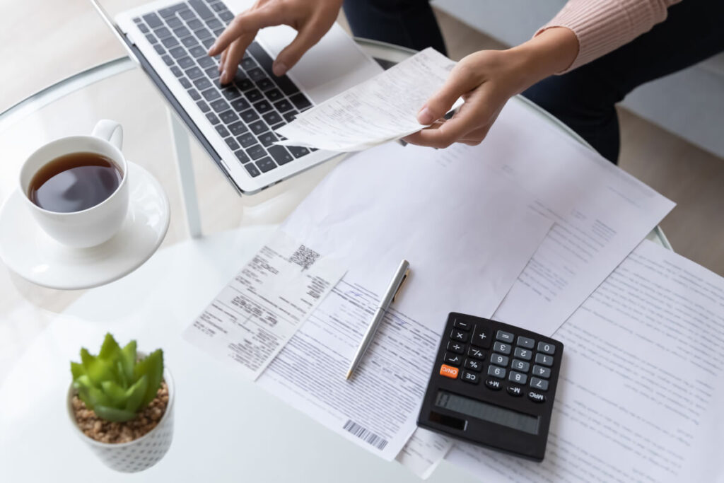 Person calculating rent on their computer with bills all around them.