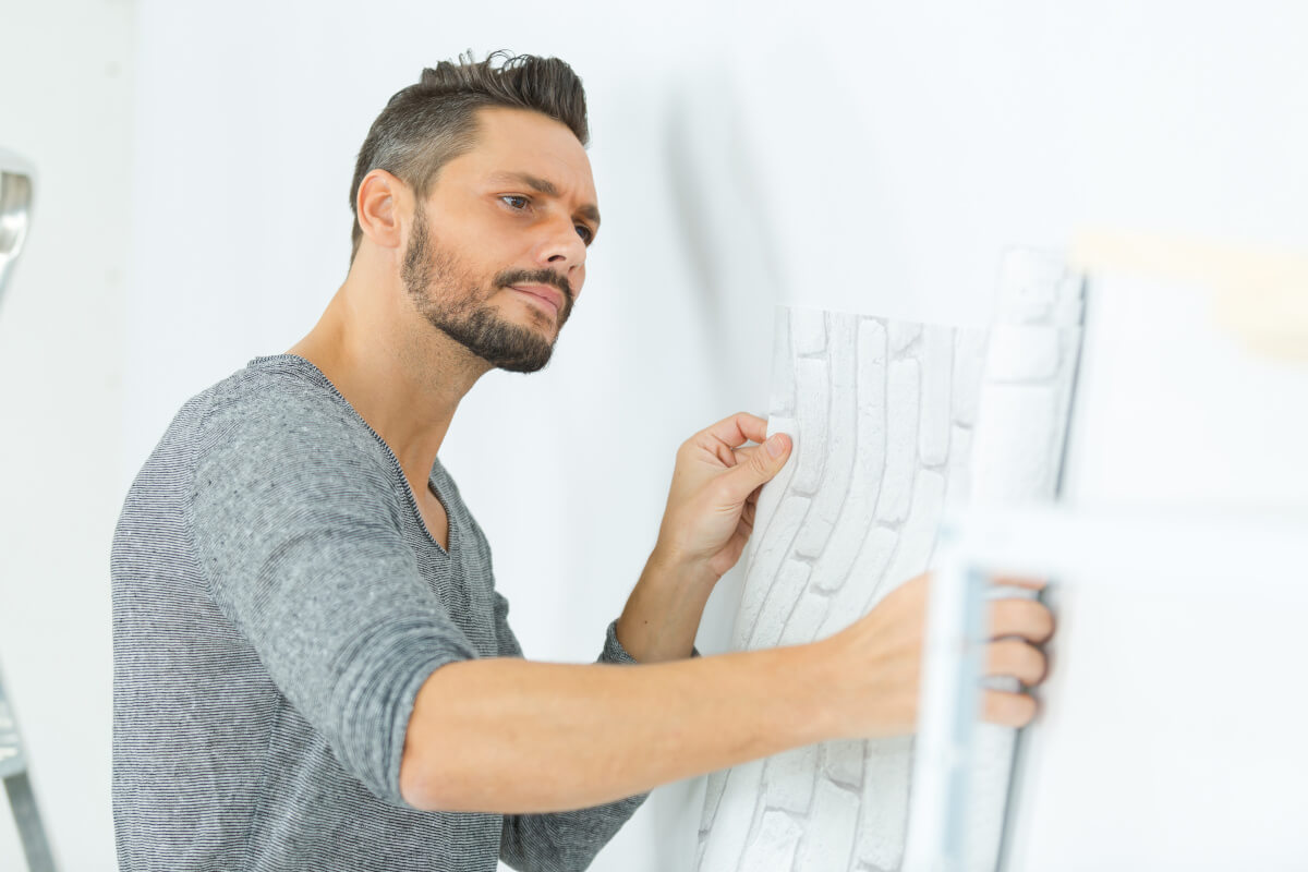 A man applies peel and stick paper to a white wall.