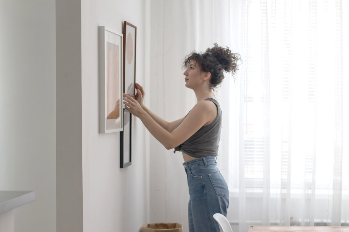 A woman hangs wall art in her apartment.