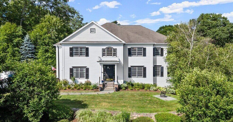 A white, two-story home on a wooded lot.