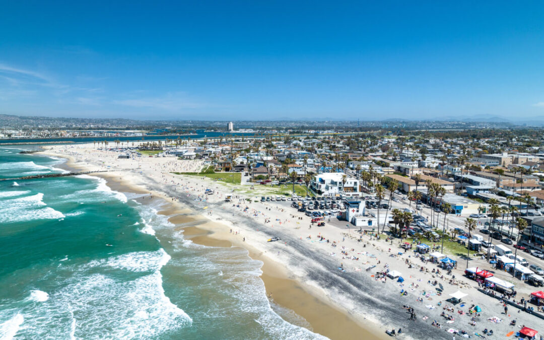 An aerial view of the Ocean Beach neighborhood in San Diego shows bright blue water along a sandy beach.