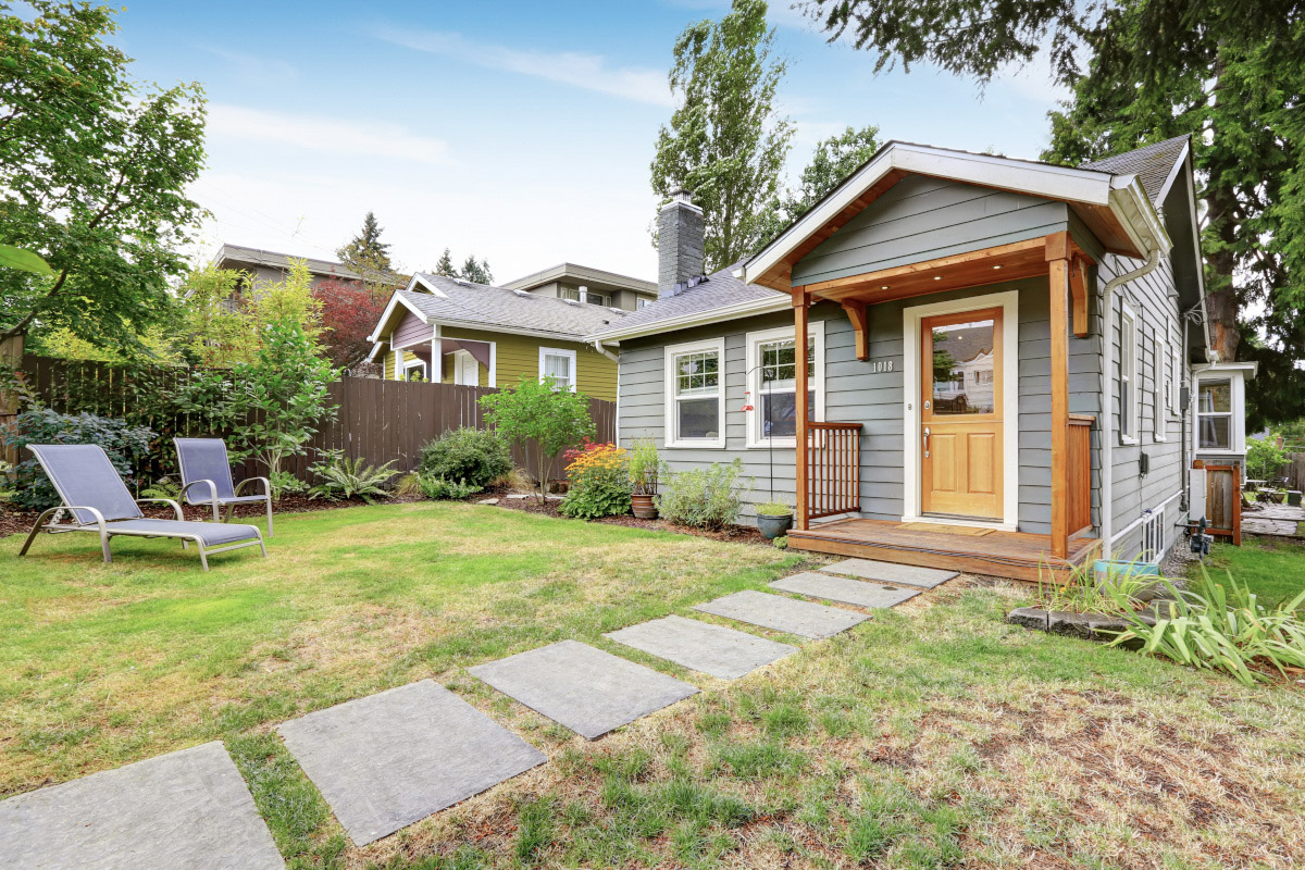 A view of a small gray cottage from a grassy back yard.