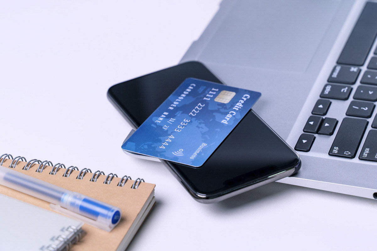 A close-up shot of a credit card resting on a smartphone next to a laptop and a notebook.