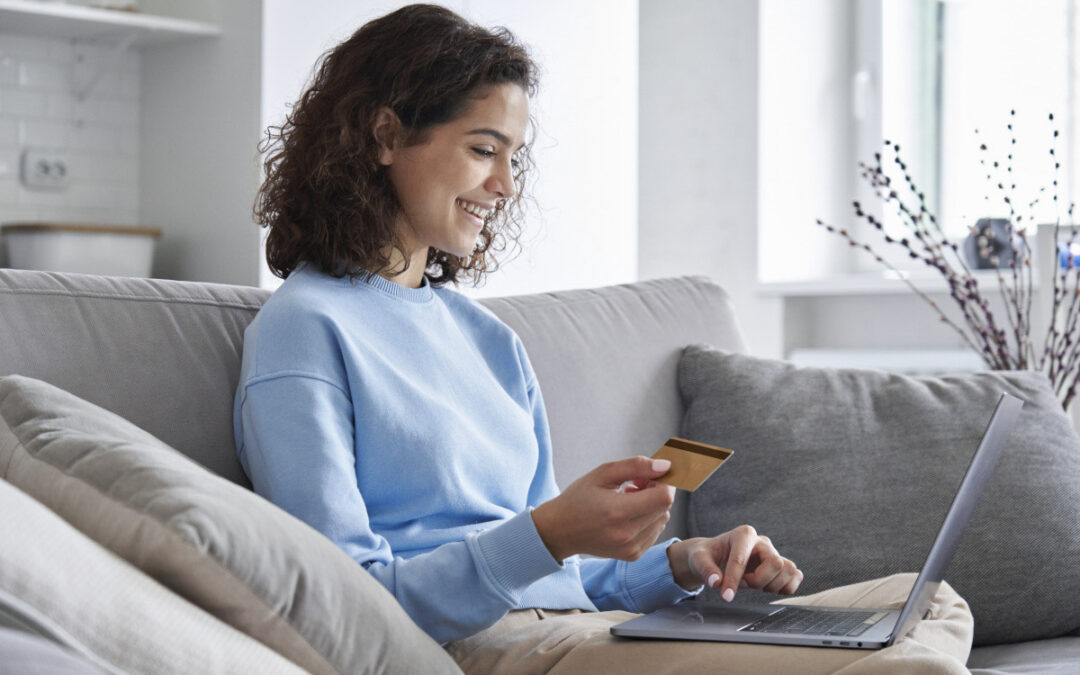 Happy young woman holding credit card and making digital payment on a laptop.